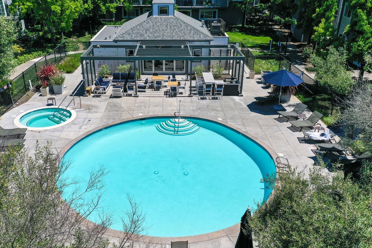 Aerial view of a large outdoor community pool with a circular spa, lounge chairs, and a shaded seating area. Explore 1 and 2 bedroom apartments and townhomes in Larkspur, CA with modern floor plans and a convenient location just a 30-minute drive from San Francisco.