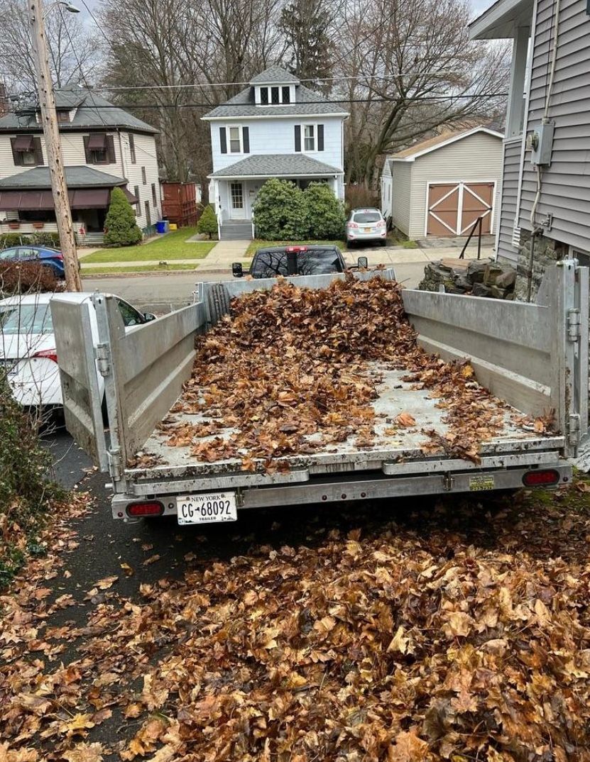 A trailer filled with leaves is parked in front of a house.