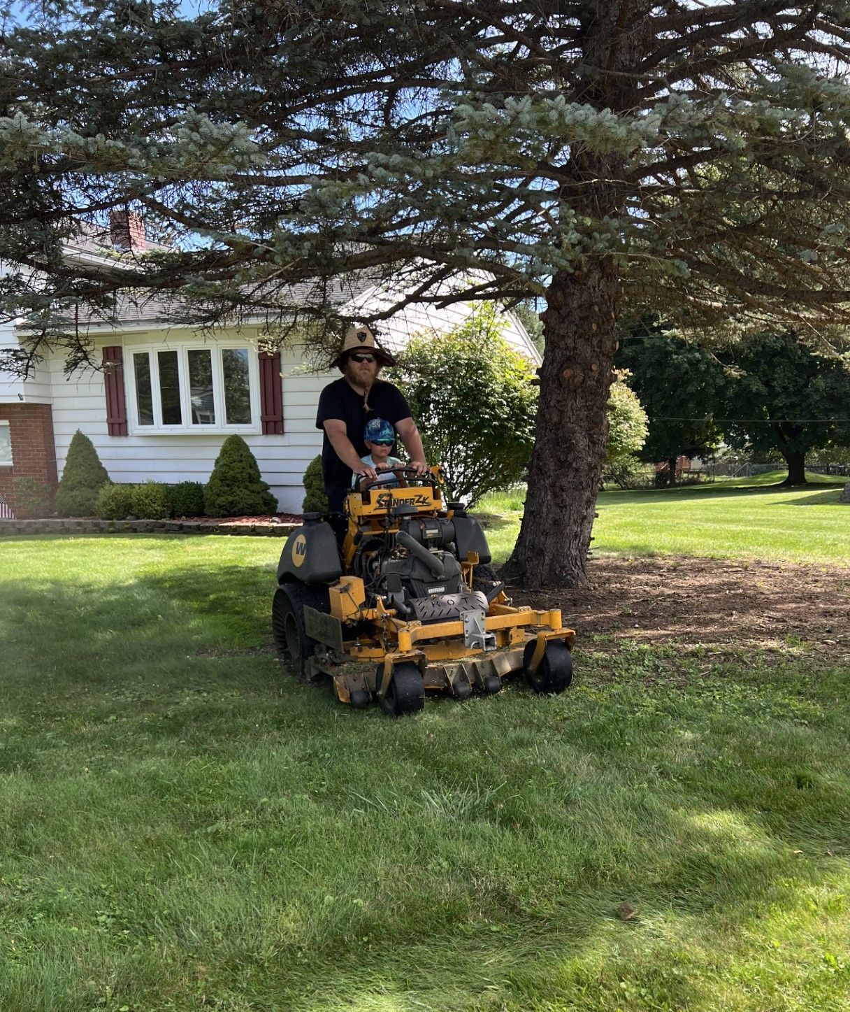 A man is riding a yellow lawn mower on a lush green lawn.