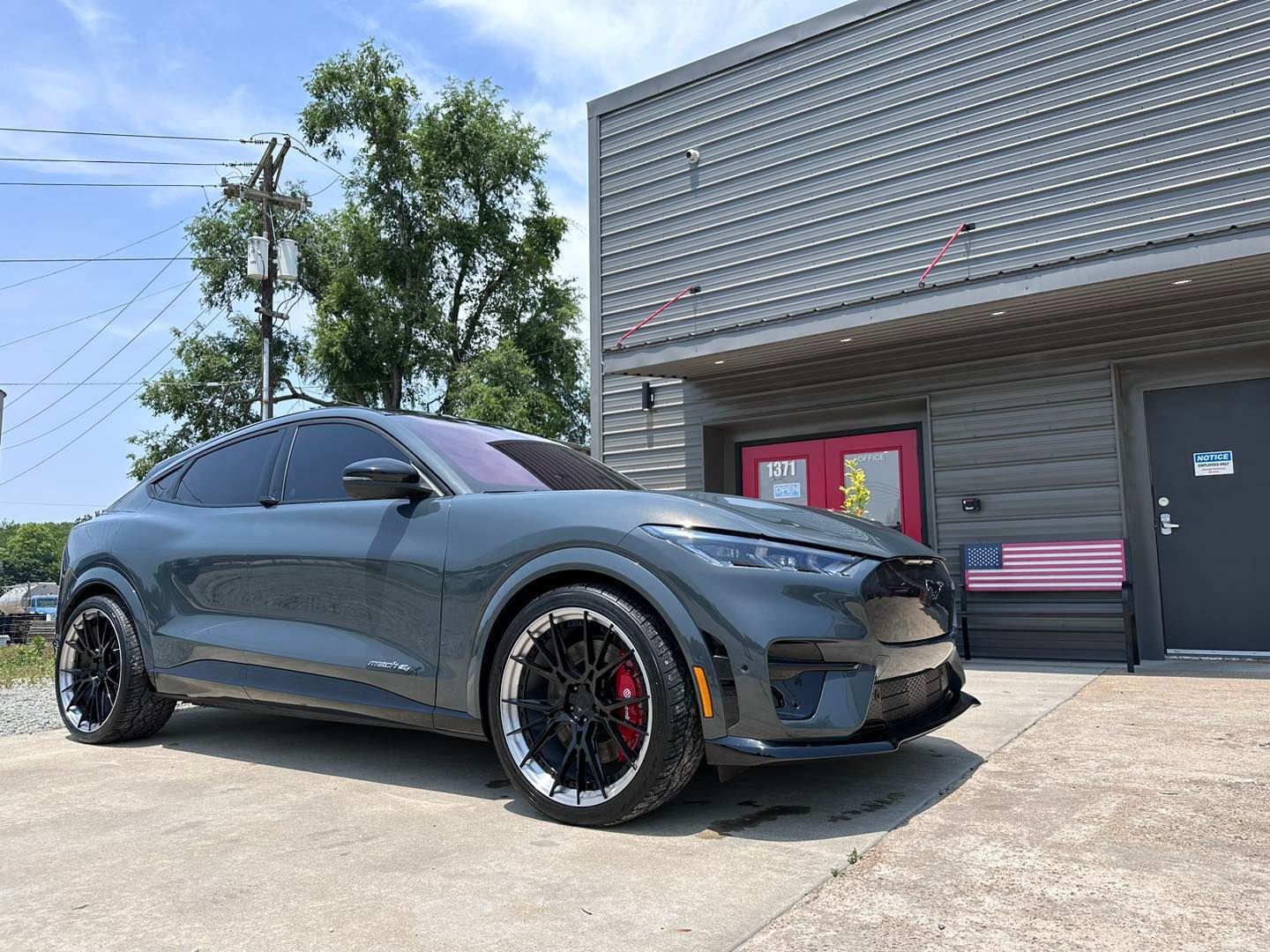 Dark gray Ford Mustang Mach-E parked in front of a gray building. Black wheels, red calipers.