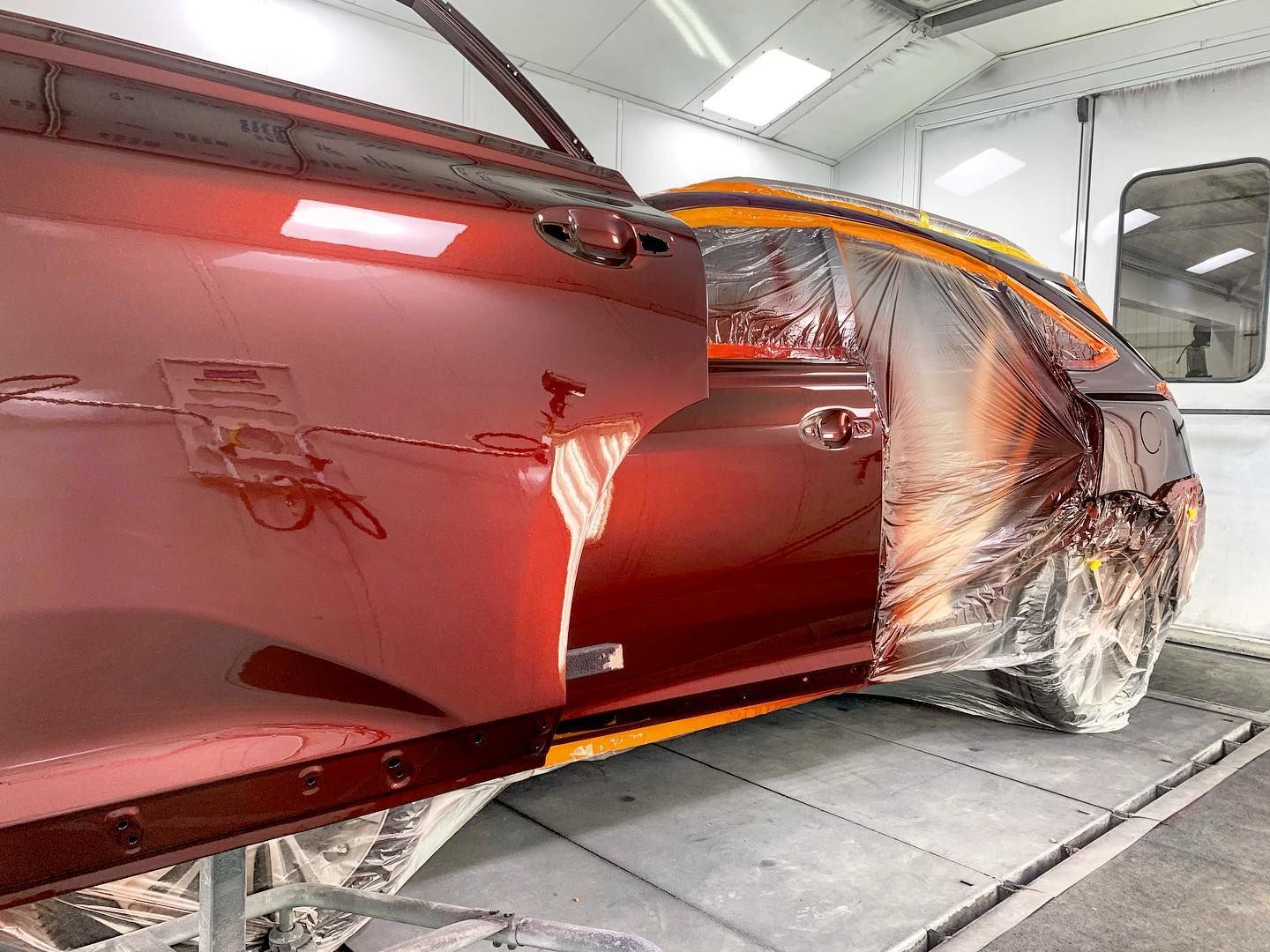 Car door being repainted red in a spray booth, masked for protection.