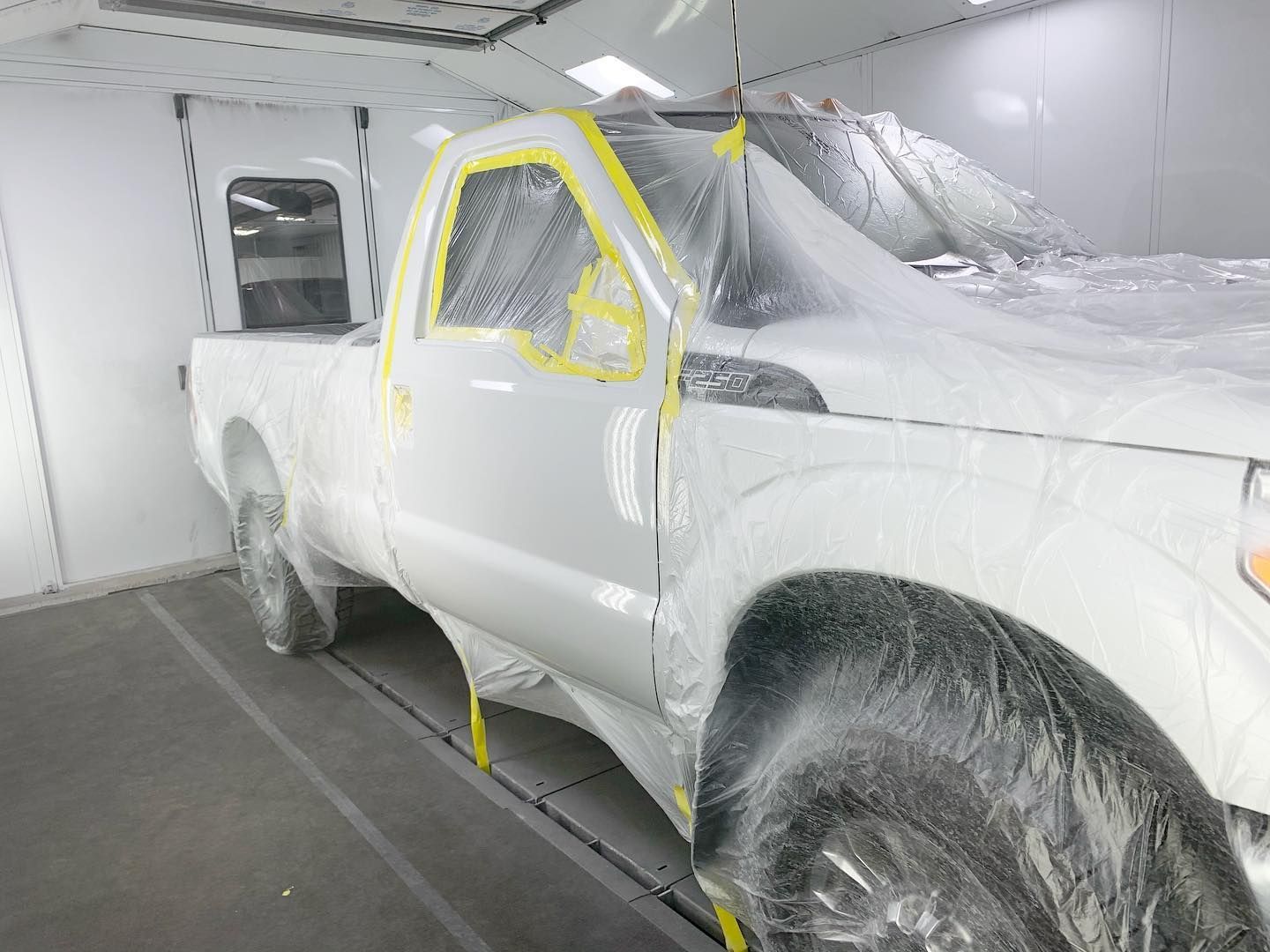 White truck in a paint booth, covered in plastic, taped off for painting.