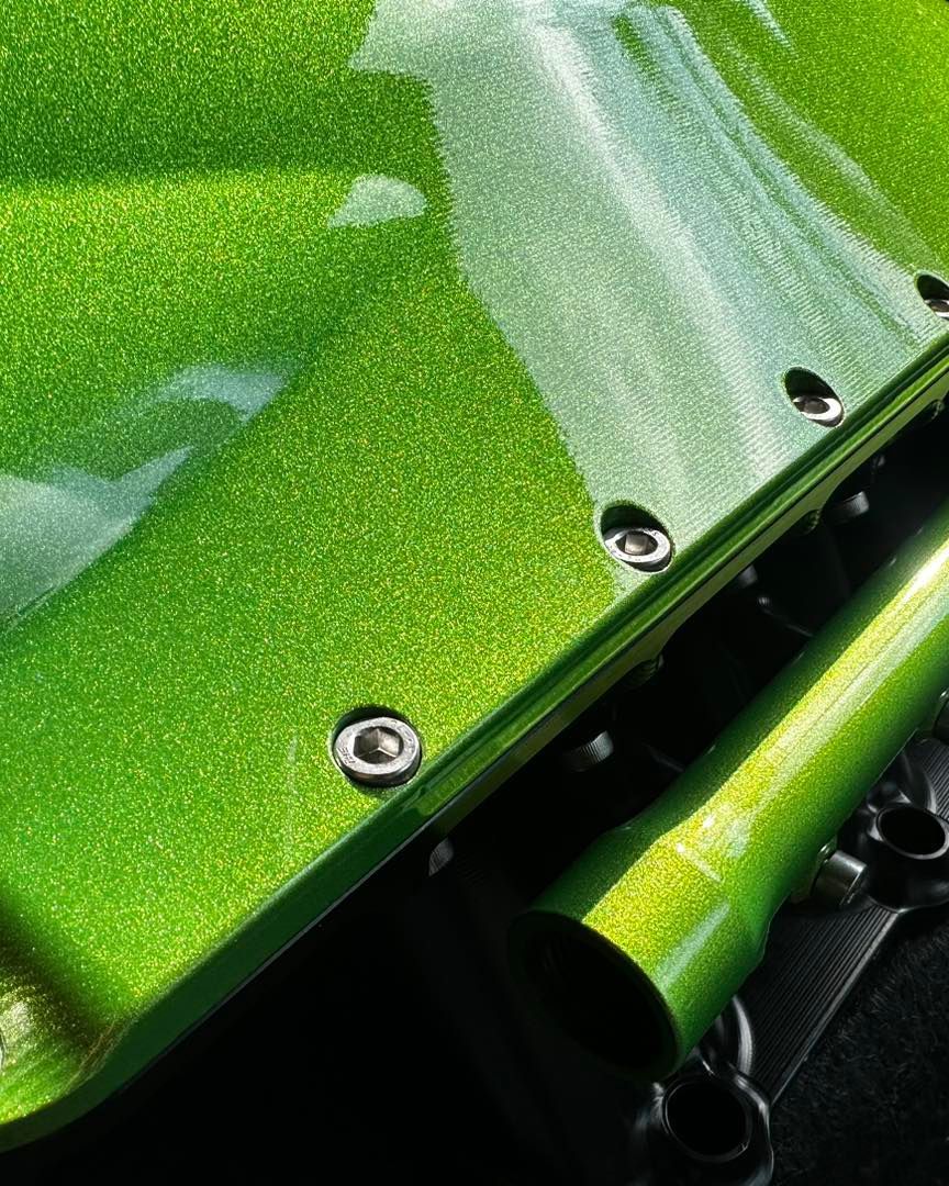 Close-up of shiny green surface with visible glitter, attached by silver bolts, next to a matching tube.