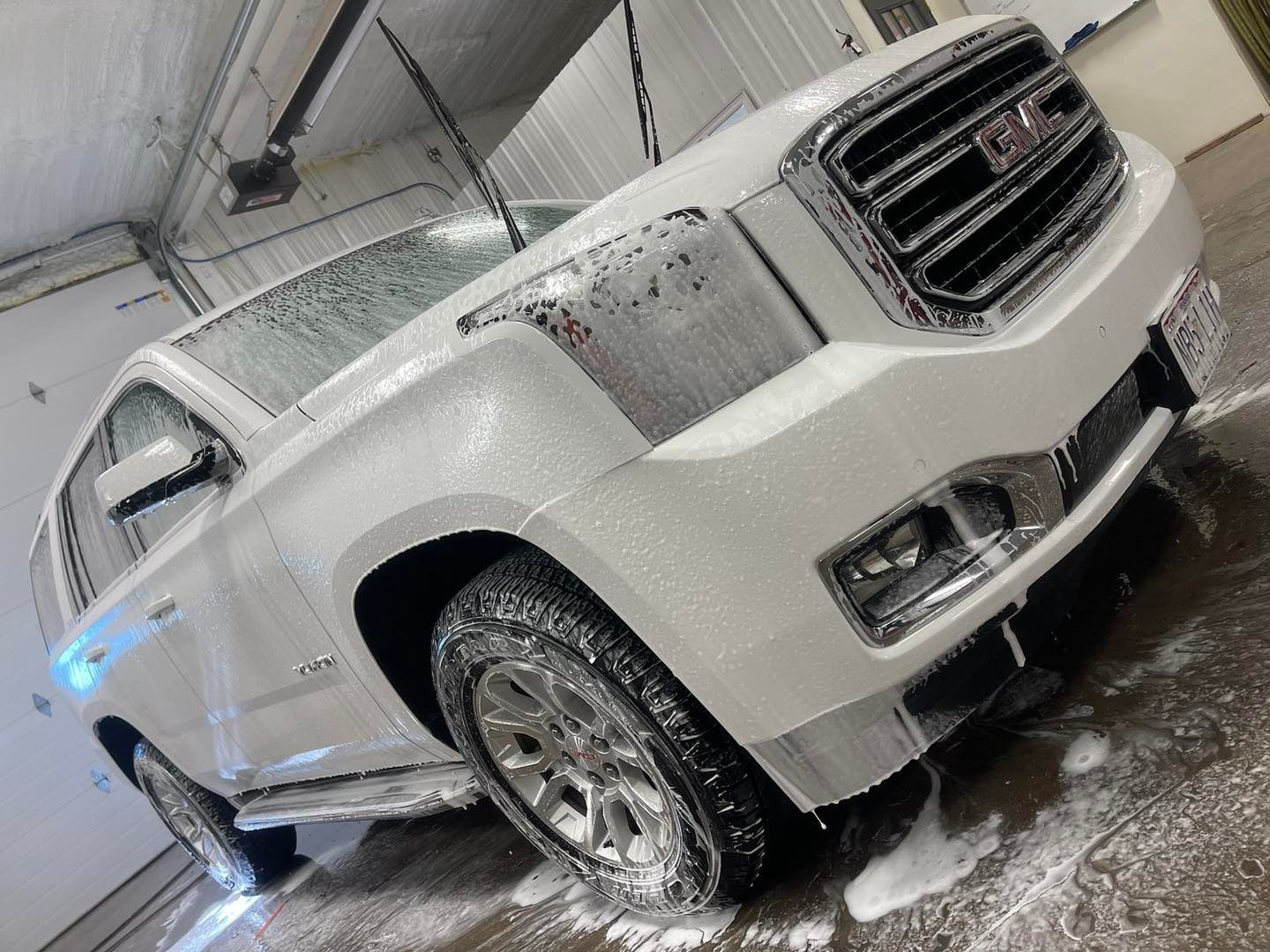 White GMC Yukon SUV covered in soapy foam at a car wash.