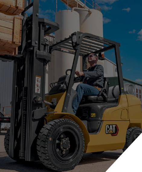 Una persona conduce una carretilla elevadora CAT amarilla al aire libre, con cajas de madera al fondo.