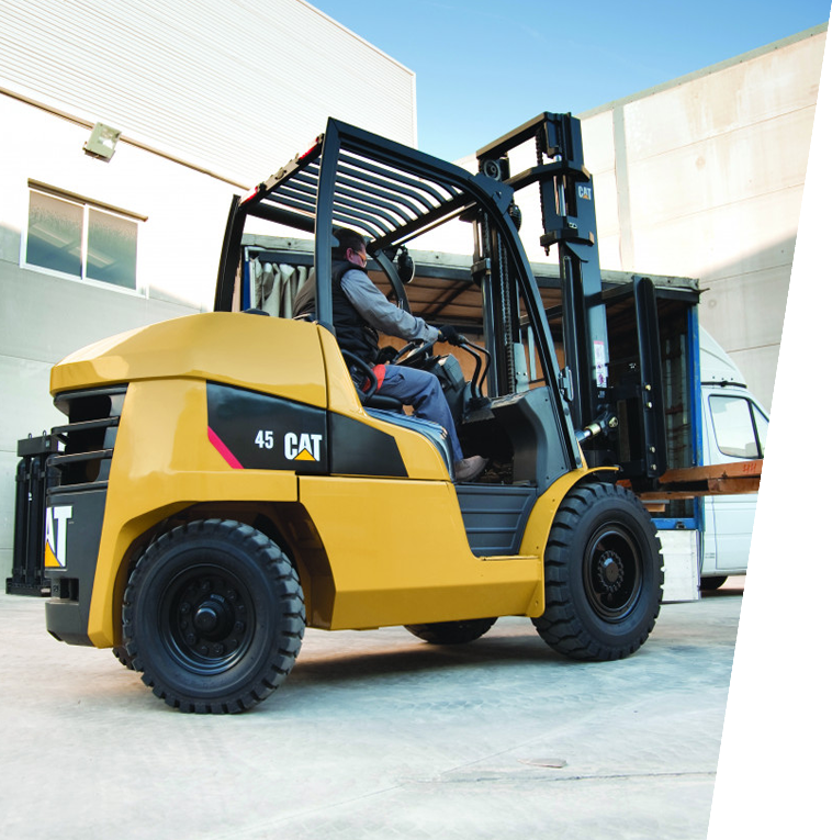 Una carretilla elevadora Caterpillar amarilla descargando un camión. Una persona la opera. Al aire libre.
