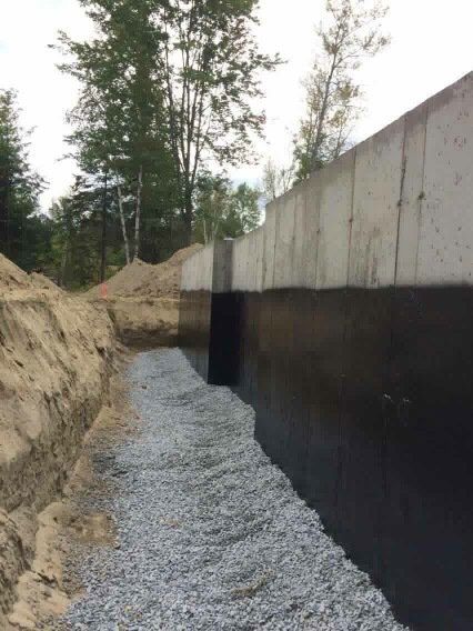 Fondations d'un bâtiment avec étanchéité noire, gravier et tranchée.