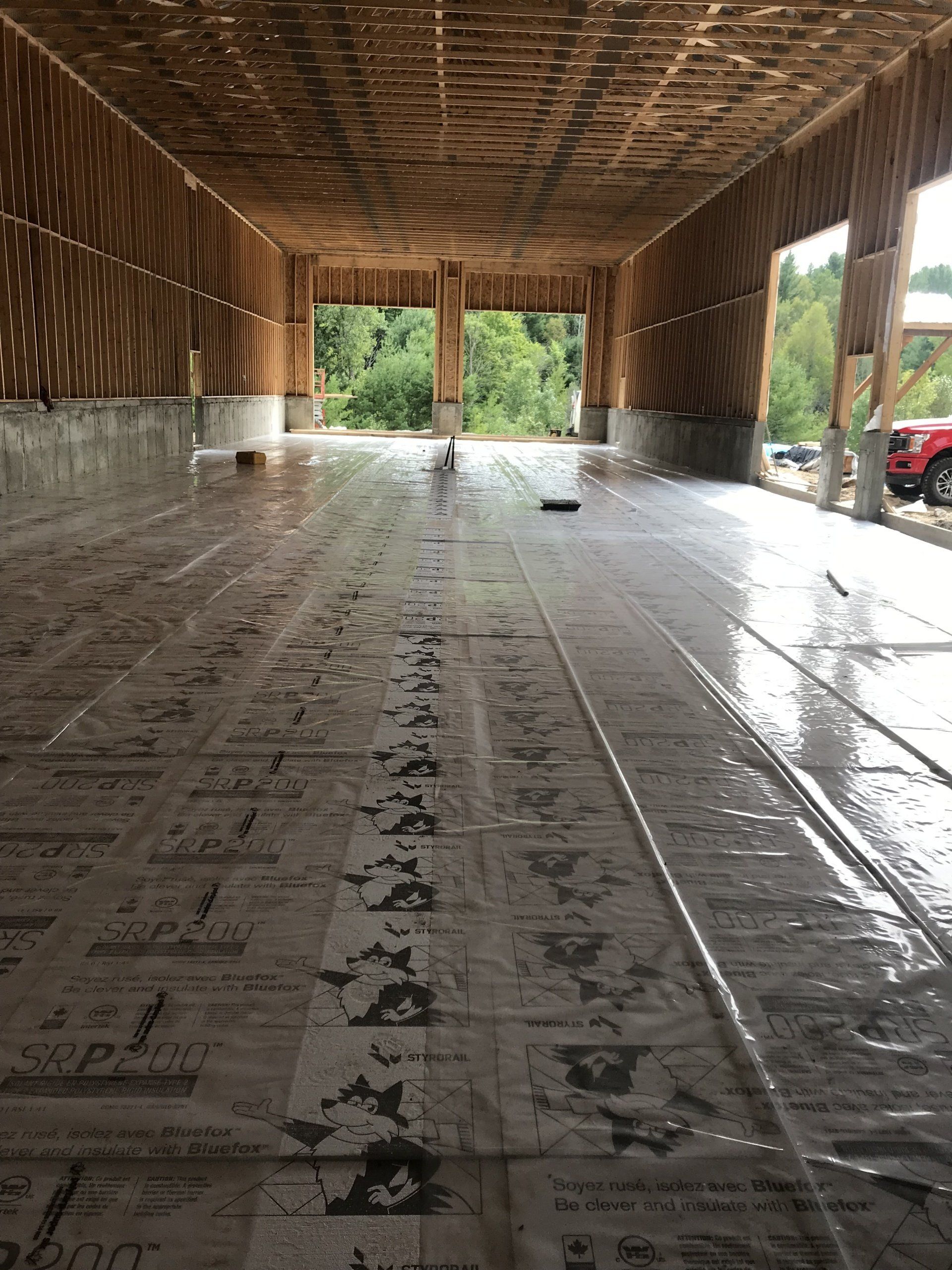 Intérieur d'un bâtiment en construction, montrant un sol en béton recouvert d'une bâche en plastique.