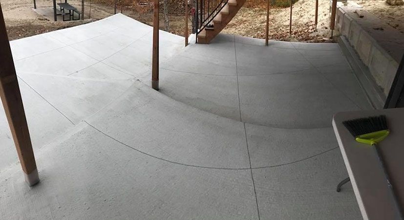 Terrasse en béton aux bords arrondis, supports en bois et escalier en arrière-plan.