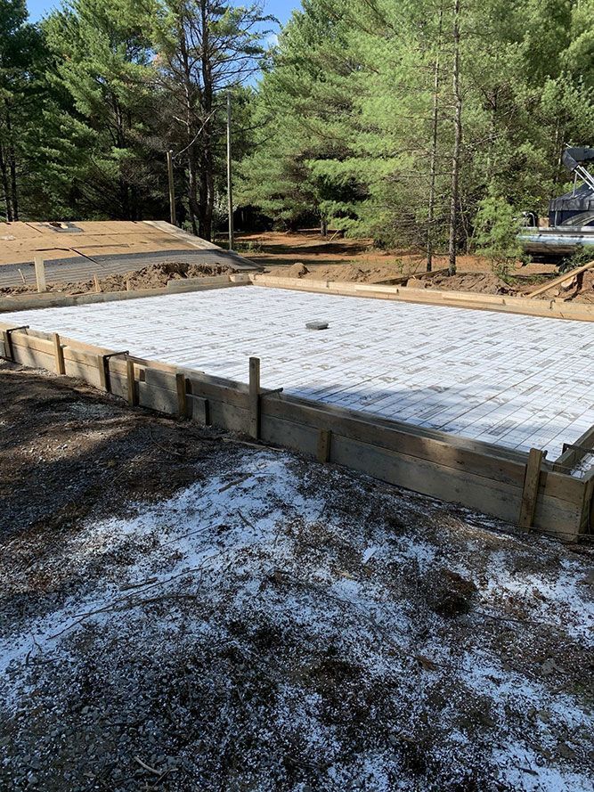 Coffrages en bois contenant de la mousse blanche pour une dalle de béton ; zone boisée en arrière-plan.