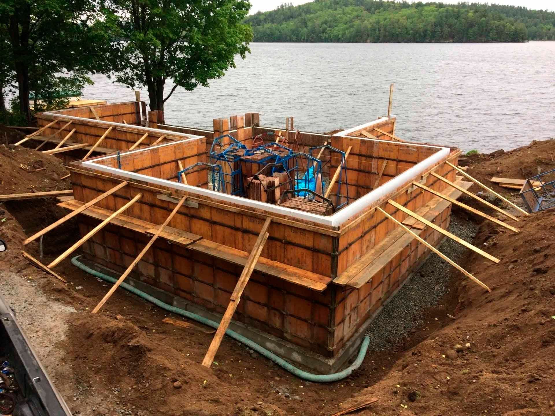 Fondations en construction près d'un plan d'eau, avec des poutres de soutien en bois.