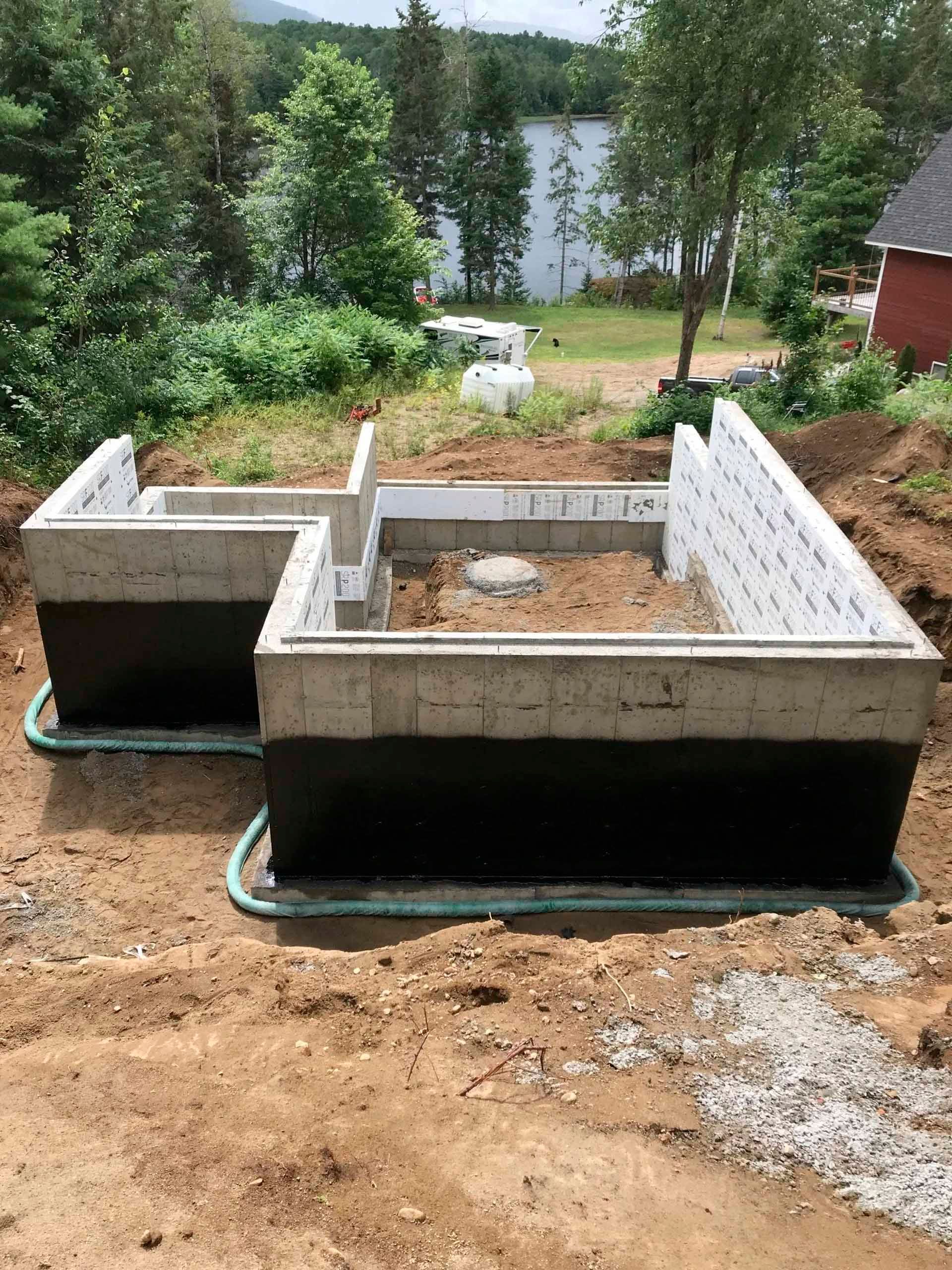 Murs de fondation en béton avec étanchéité noire, entourés de terre et de gravier.