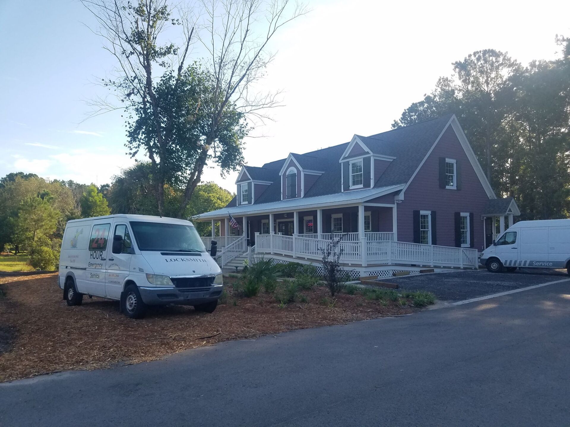 Two white vans are parked in front of a large brick house.