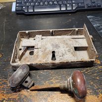 A key and a lock are sitting on a wooden table next to a keyboard.