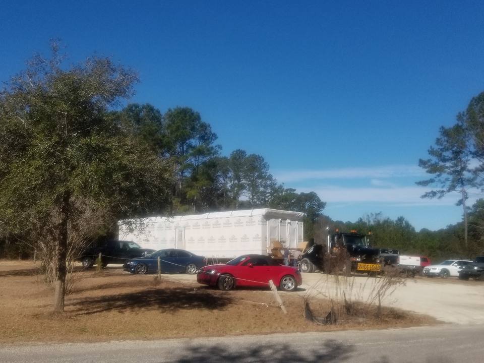 A red car is parked in a parking lot next to a white trailer.