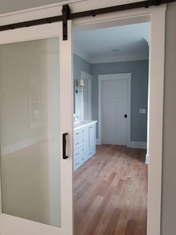 A sliding barn door is open to a bathroom with hardwood floors.
