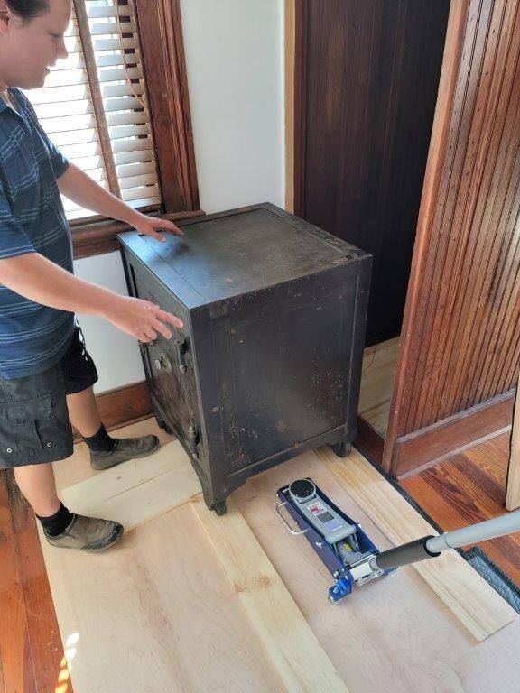 A man is standing next to a safe on a wooden floor.