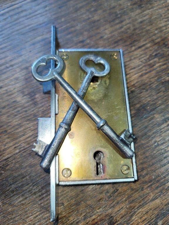 Two keys are crossed over a brass lock on a wooden table.