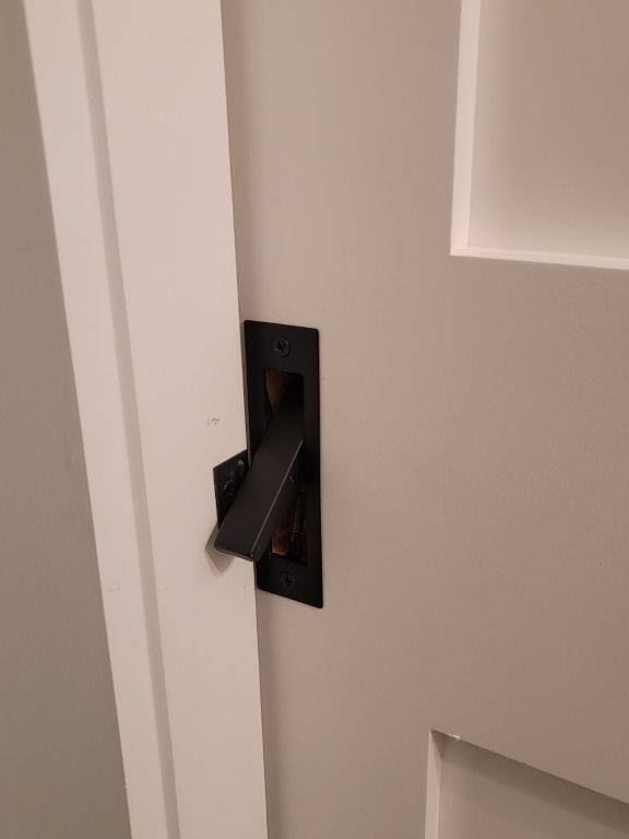 A close up of a black door handle on a white door.