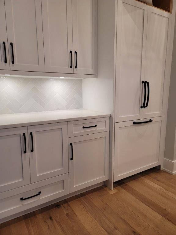 A kitchen with white cabinets and black handles and a wooden floor.