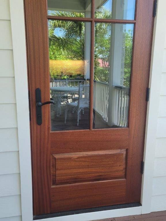 A wooden door with a glass window is open to a porch.