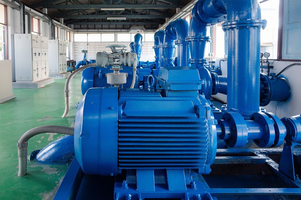 A large blue motor is sitting in a room surrounded by blue pipes.