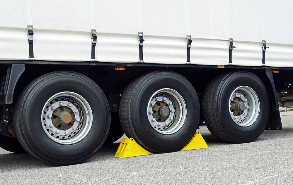 Three Truck Tires With Yellow Wheel Chocks On Pavement Near A White Trailer — Canobolas Canvas In Orange, NSW