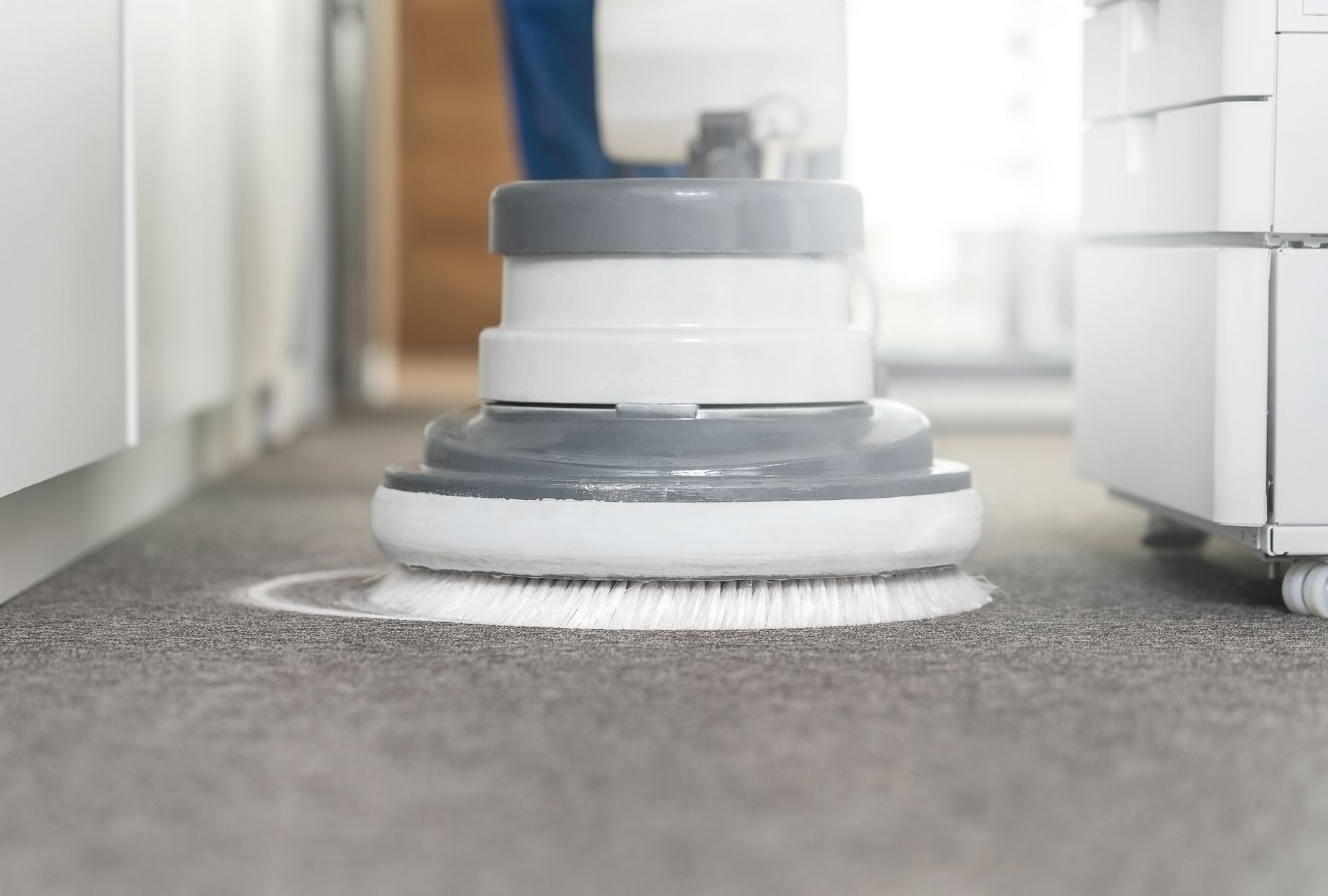 A person is cleaning a carpet with a machine in an office.