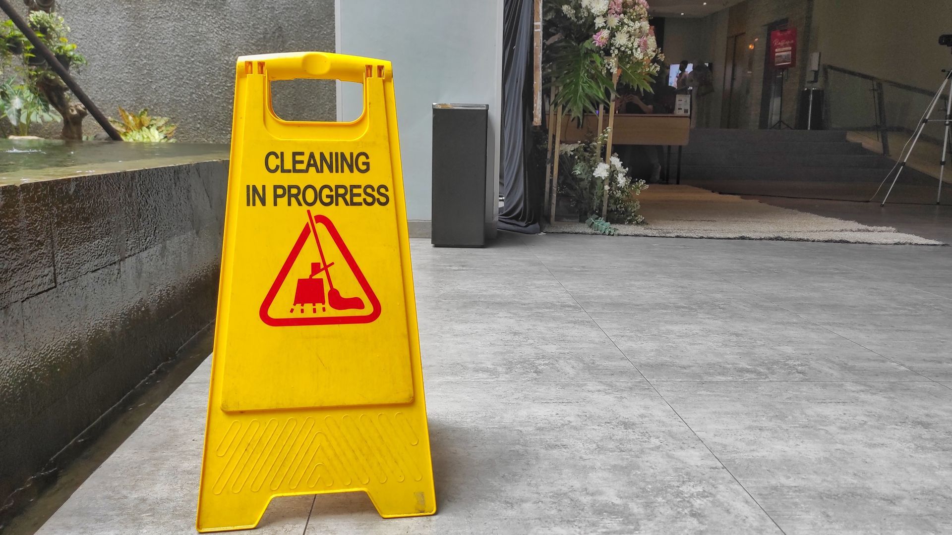 A yellow caution sign is sitting on the sidewalk in front of a building.