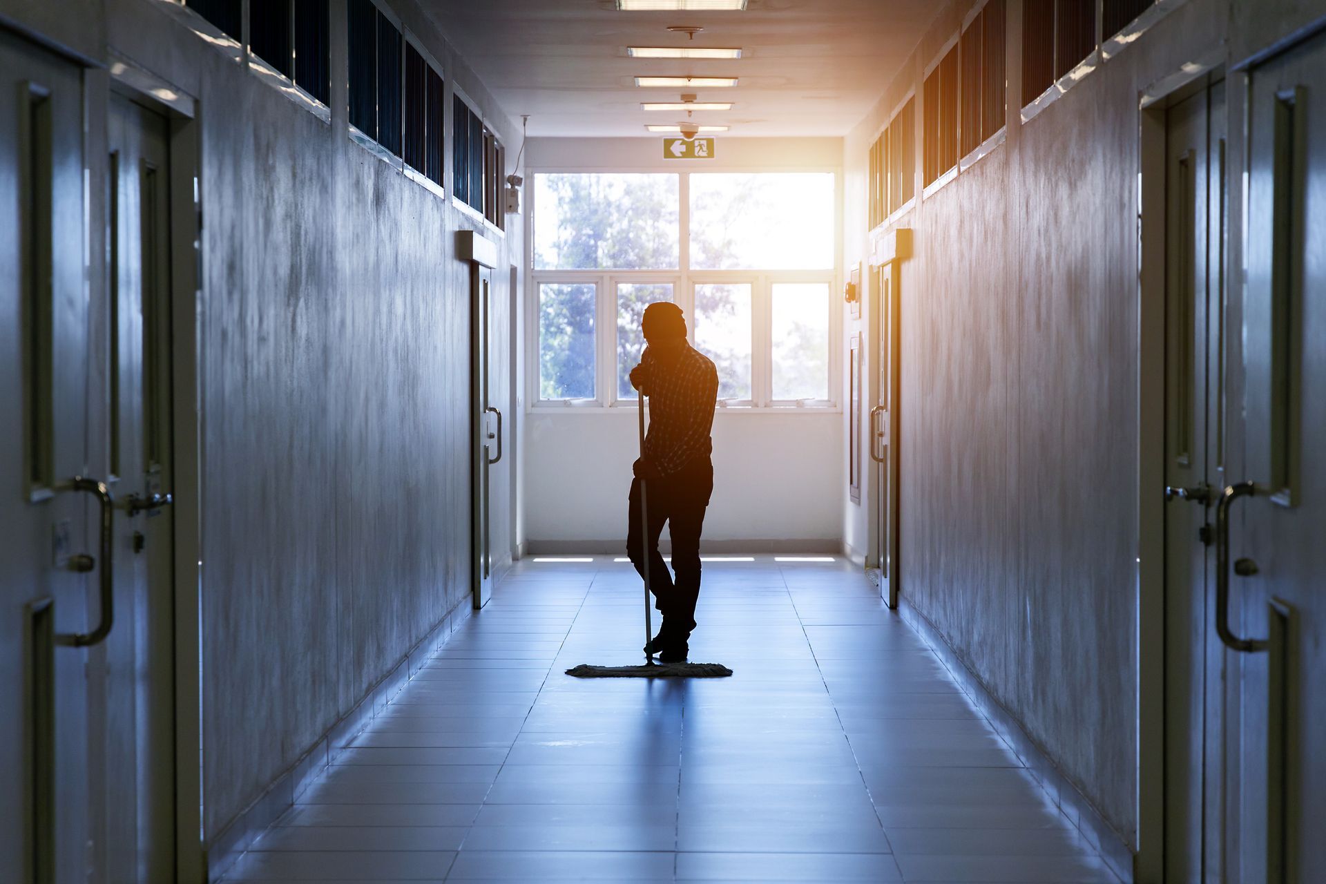 A man is cleaning the floor of a hallway with a mop.