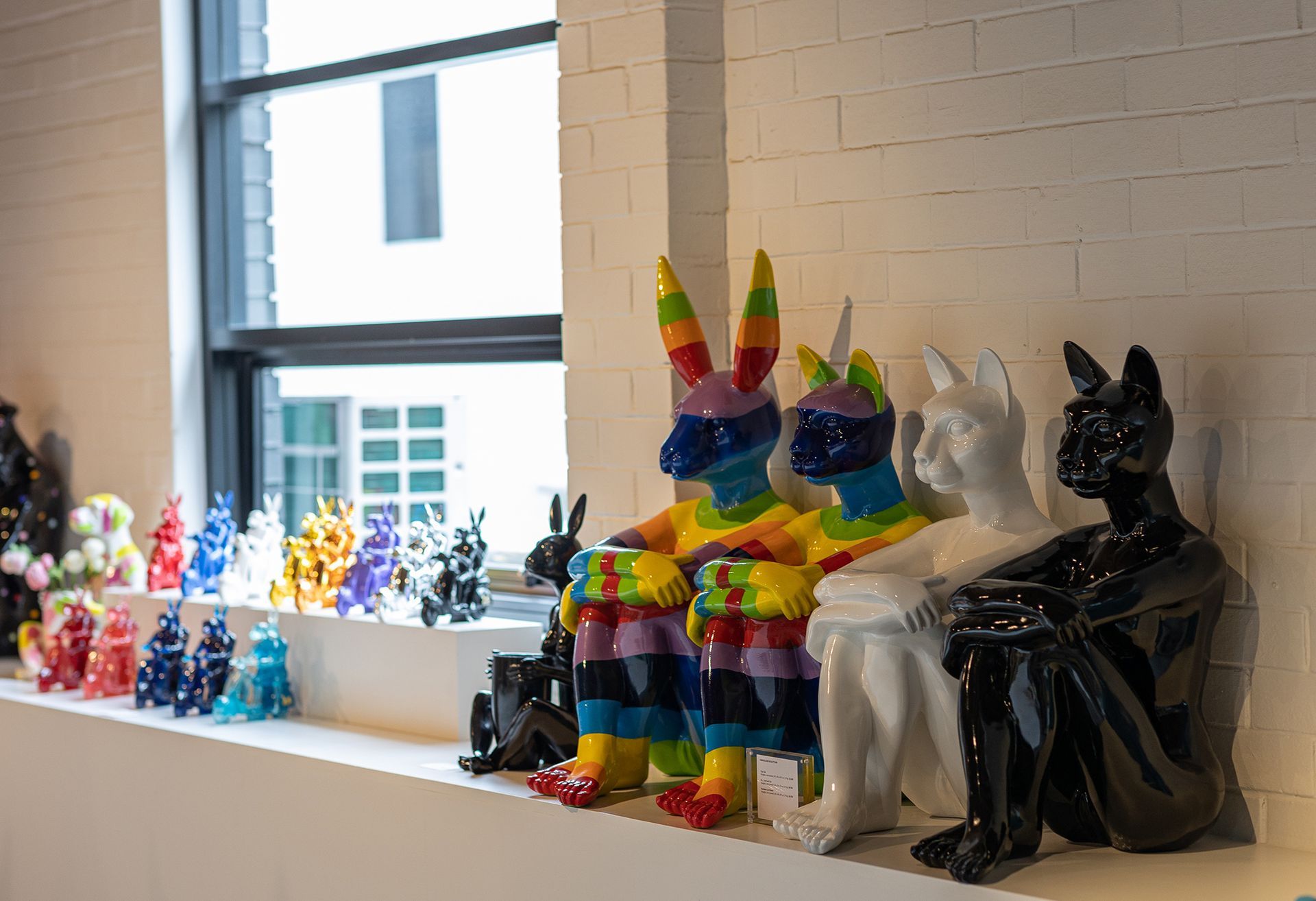 A bunch of sculptures are sitting on a shelf in front of a window.