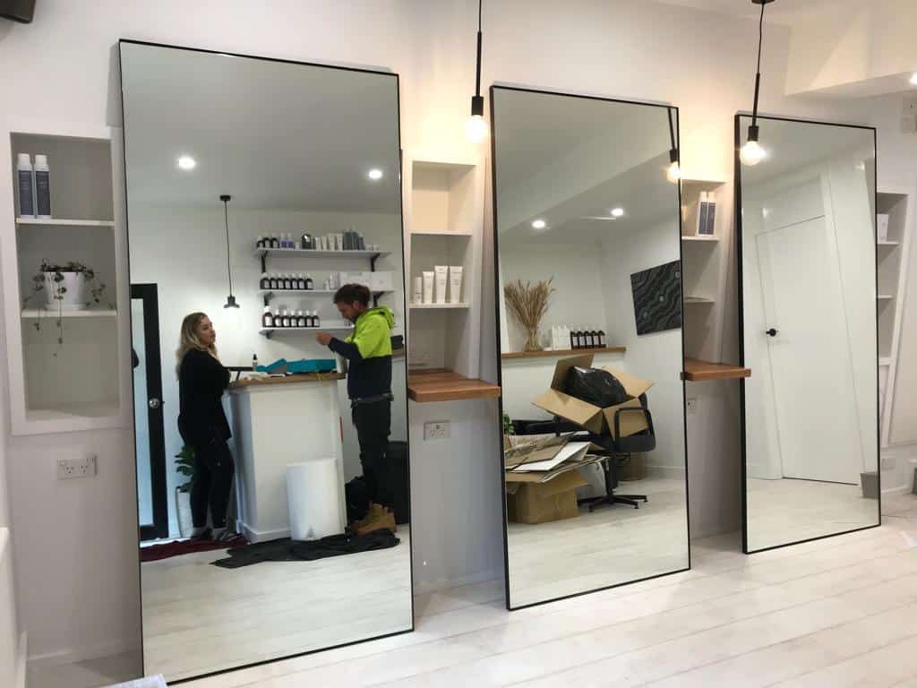 A woman is standing in front of a large mirror in a salon.