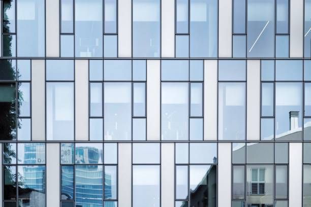 Modern glass building facade with reflections of cityscape and trees.