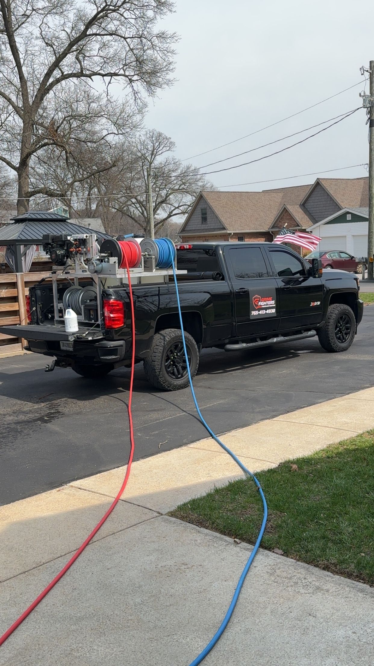 A black pickup truck parked in a driveway, outfitted with pressure washing equipment, hoses, and an engine in the truck bed.