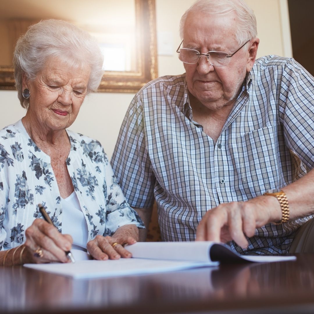 Elderly couple reviewing and signing a document together, seated at a table.