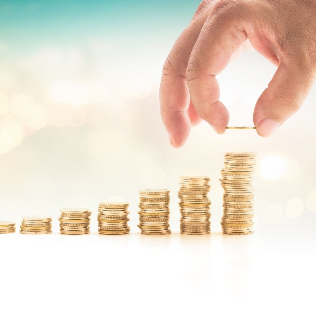 Hand adding coin to growing stacks of gold coins.