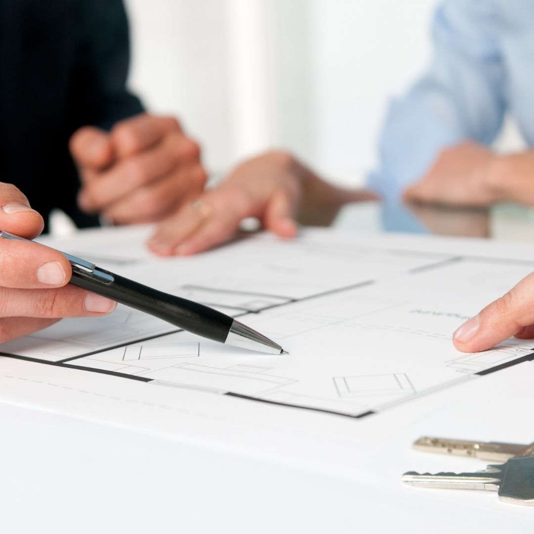 Hands pointing at blueprints, a pen and keys on a table, discussing a property plan.