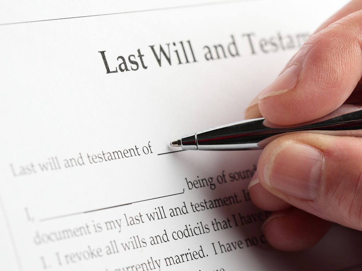 Hand signing a Last Will and Testament document with a pen.