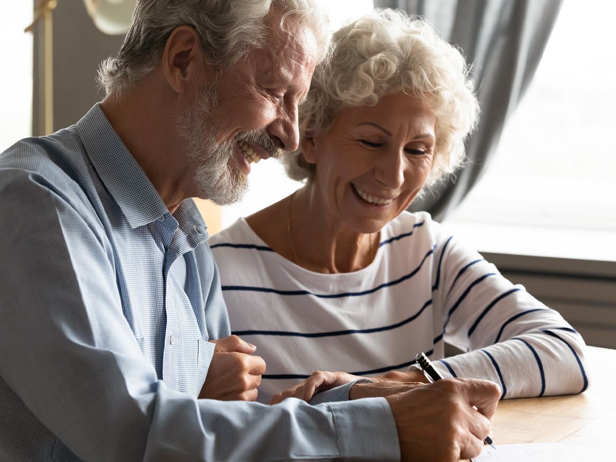 Senior couple smiling, looking at and signing a document together indoors.