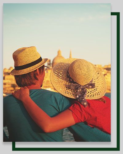 Couple embracing, looking at a building with domes; wearing hats, turquoise and red shirt, sunny day.