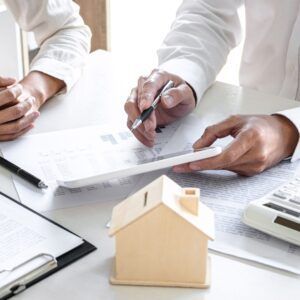 Two people reviewing documents, with a model house and calculator on a table.