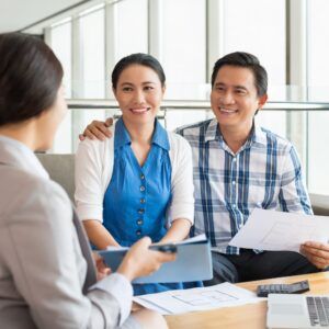 Couple smiling, reviewing paperwork with an advisor, seated indoors.