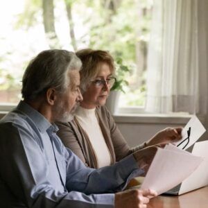 Older couple reviewing documents at a table near a window. One woman wears glasses.
