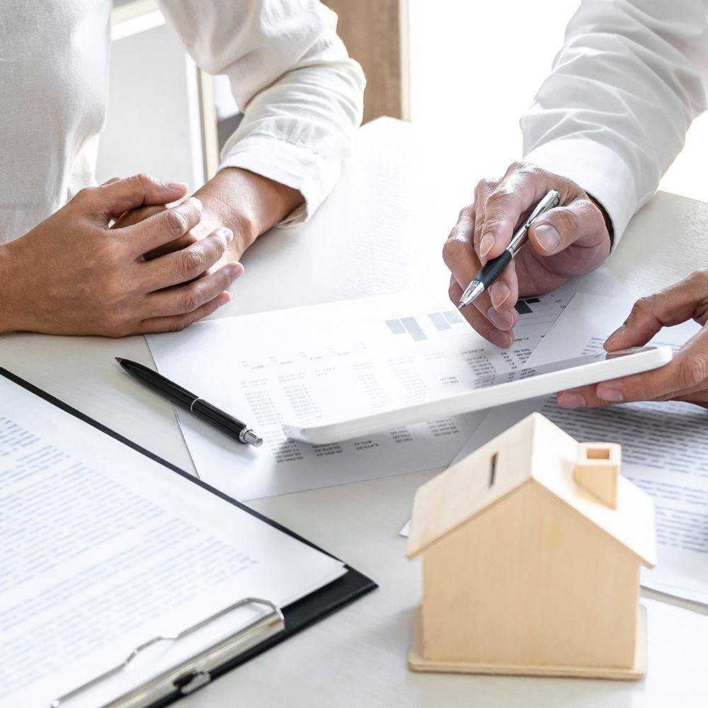 Person reviewing documents with another person, small house model on the table.
