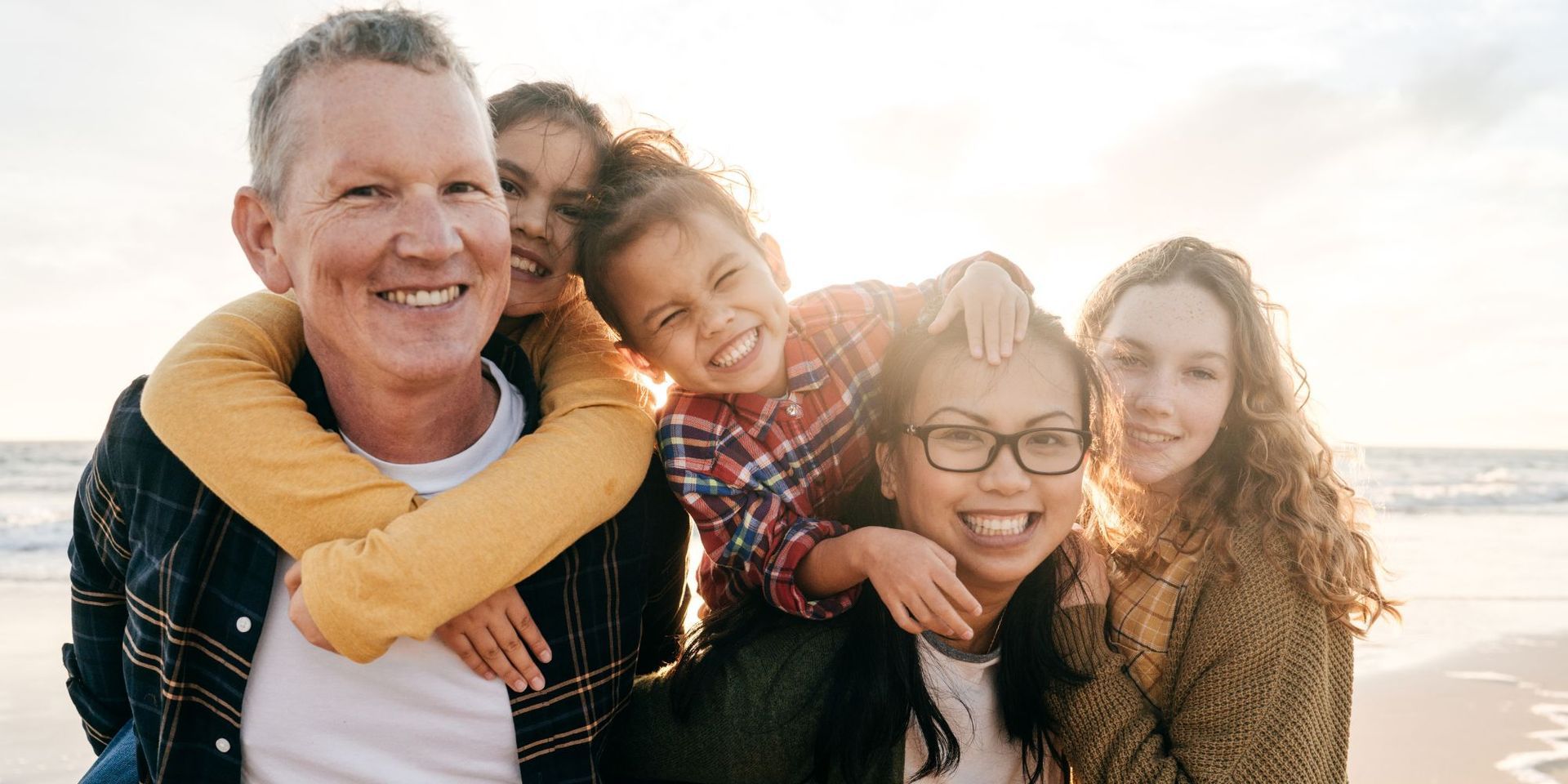 Family smiling together on a beach, lit by sunlight.