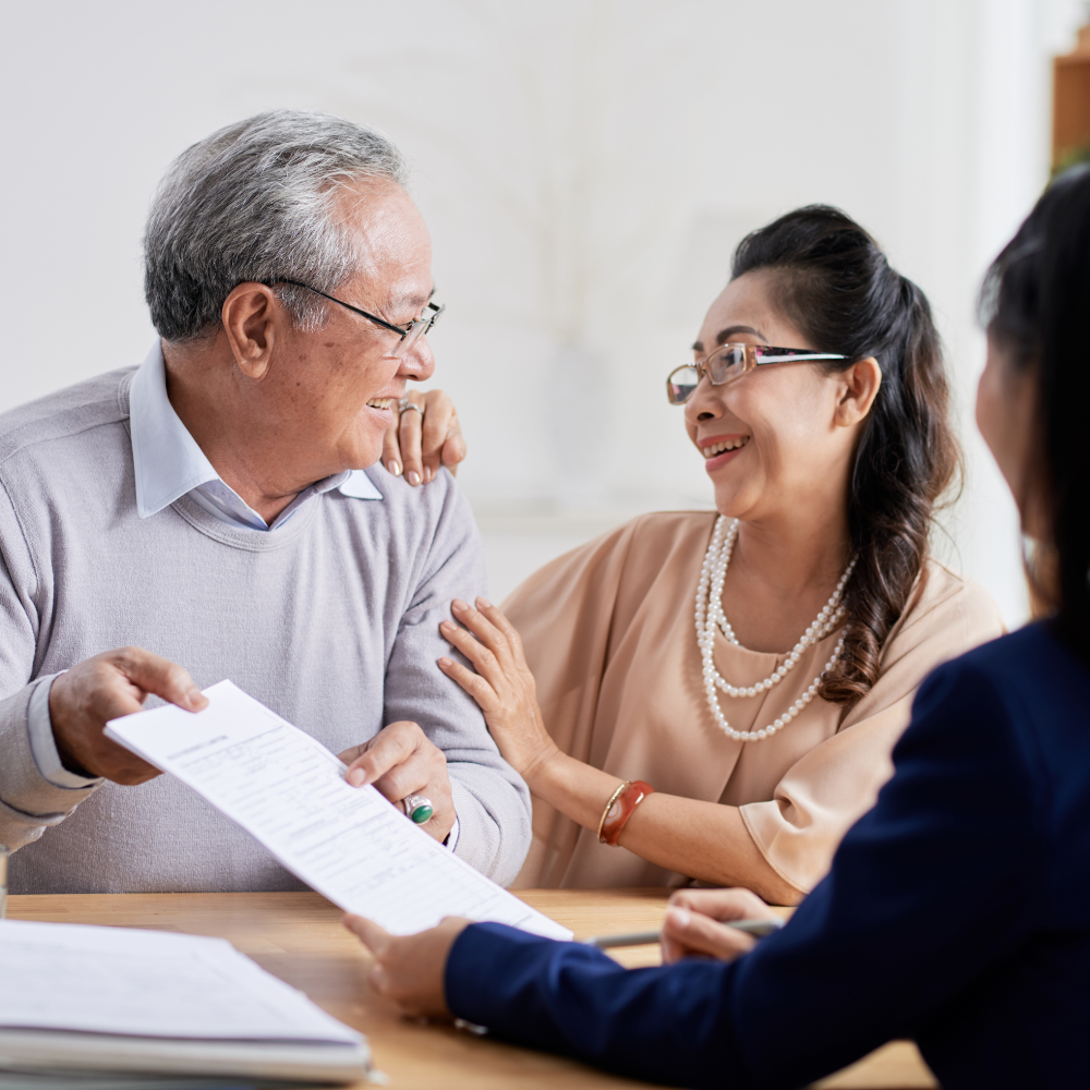 Senior couple reviewing paperwork with a professional. They smile while seated at a table.