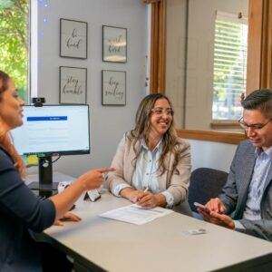 Three people in a meeting at a desk, reviewing documents.