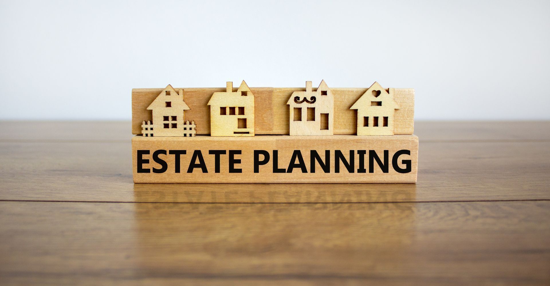Wooden block with “ESTATE PLANNING” text and miniature houses on a wooden surface.