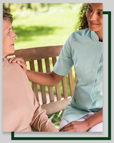 Caregiver comforts person on a bench outdoors, hand on shoulder.