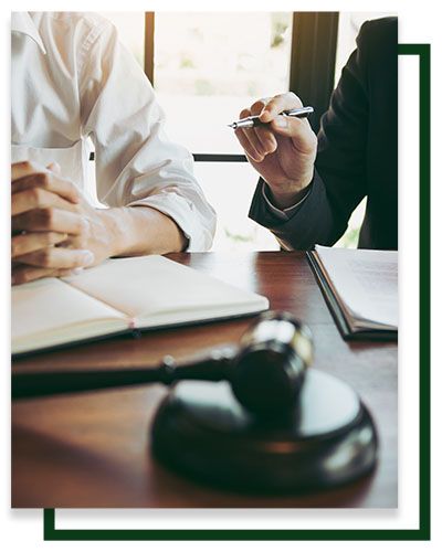 Person in white shirt and lawyer with a gavel, pen, and open book, discussing at a wooden table.